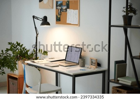 Desk of fashion design student with laptop, lamp and moodboard on wall