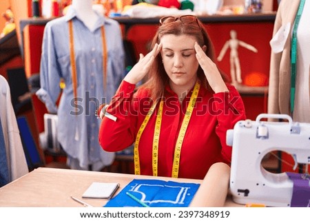 Young beautiful plus size woman tailor stressed sitting on table at atelier Royalty-Free Stock Photo #2397348919