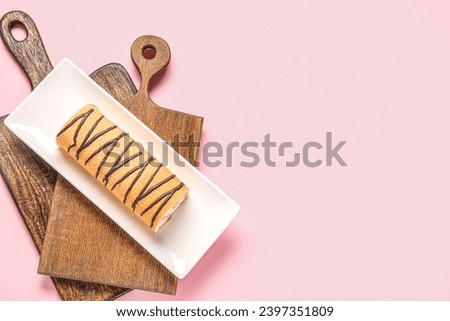 Plate with sweet sponge cake roll on pink background
