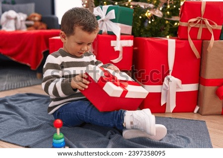 Adorable caucasian boy unpacking christmas gift sitting on floor at home