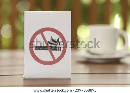 No Smoking sign and cup of drink on wooden table against blurred background, closeup
