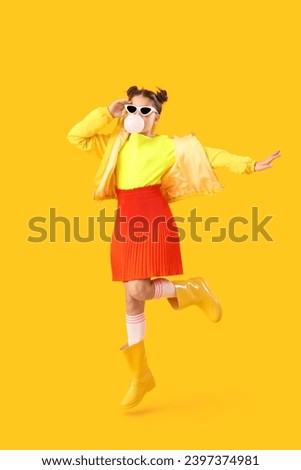 Trendy girl blowing bubble gum while jumping on yellow background