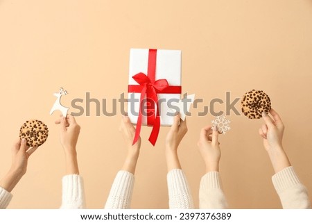 Hands holding gift box, cookies and Christmas decor on beige background
