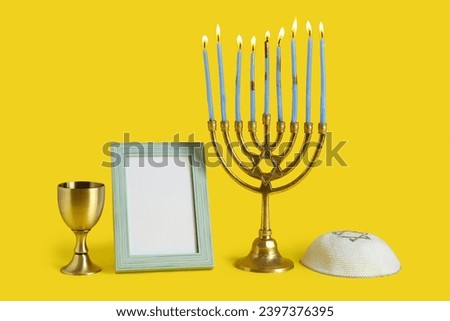 Menorah, kippah, blank picture frame and cup for Hanukkah celebration on yellow background