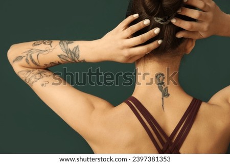 Tattooed young woman on green background, back view