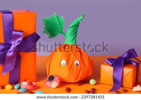 Paper pumpkin for Halloween, gift boxes and tasty candies on color background, closeup
