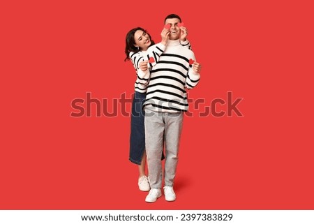 Loving young couple with paper hearts on red background. Celebration of Saint Valentine's Day Royalty-Free Stock Photo #2397383829