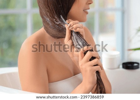 Young brunette woman applying hair product in bathroom, closeup Royalty-Free Stock Photo #2397386859