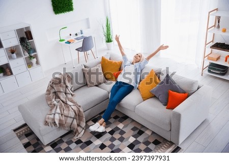 Photo portrait of attractive pensioner woman raise hands have fun sit sofa living room modern interior decoration