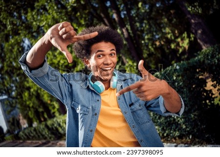 Photo of funky excited guy dressed jeans shirt headphones showing photo gesture outdoors urban city park