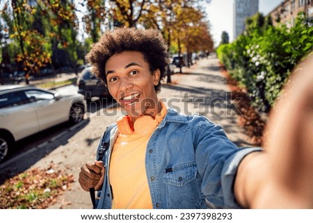 Photo of cheerful tricky guy dressed jeans shirt headphones tacking selfie stick out outdoors urban city park Royalty-Free Stock Photo #2397398293