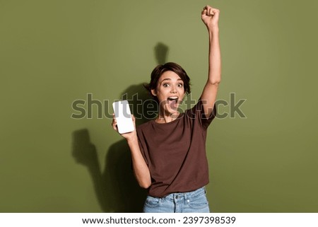 Photo portrait of attractive young woman fist winner device white screen dressed stylish brown clothes isolated on khaki color background