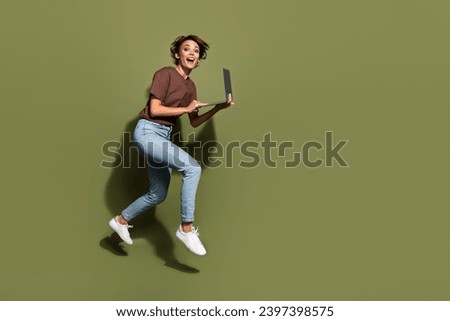 Full length photo of lovely young lady jump running hold netbook excited dressed stylish brown garment isolated on khaki color background