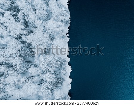 Aerial view of blue water sea and snow covered trees woods in winter Finland.