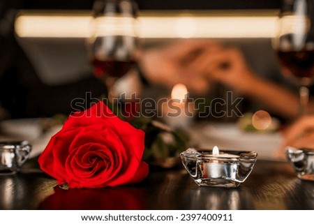 Romantic dinner date at night with focus on red rose and candles on the foreground. Defocused image of romantic relationship, dating. Valentine`s Day anniversary celebration