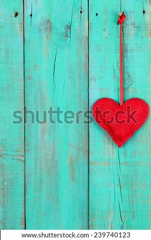 Red fabric heart hanging by red ribbon on antique teal blue wood background; Valentine's Day and Christmas background with copy space