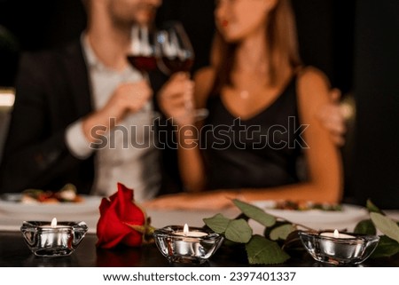 Romantic dinner date at night with focus on rose and candles. Defocused image of young couple celebrating date, anniversary, Valentine`s day in restaurant. Love and care