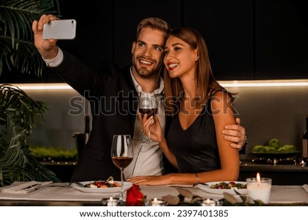 Happy couple having dinner and taking selfie using smartphone indoors. Vlogging and blogging for social media on a romantic date. Anniversary celebration.