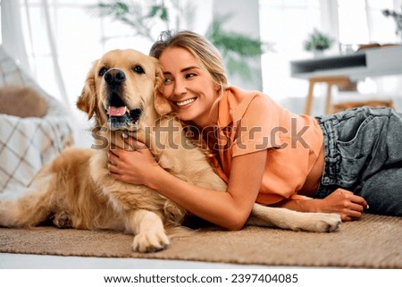 My best friend.Smiling young woman engaging in heartfelt cuddle with her furry companion at living room. Attractive woman sitting on floor and leaning head to head of lovely golden retriever. Royalty-Free Stock Photo #2397404085