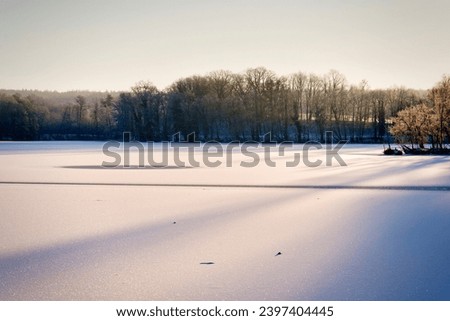 At the onset of night, a German winter scene captivates with a snow-covered field, the diminishing sunlight creating a tranquil atmosphere, enhancing the enchanting beauty of the frozen landscape.