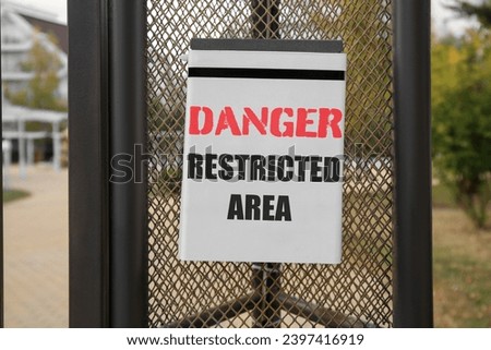 Sign with text Danger Restricted Area on fence outdoors