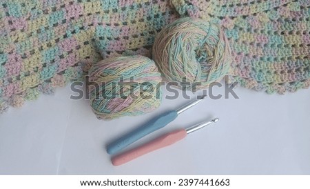A pastel-colored crochet shawl drapes gracefully, complemented by two matching yarn balls and hook sticks. 