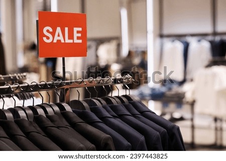 Closeup of sale banner advertising big discount for pieces of clothing displayed on rail at shop
