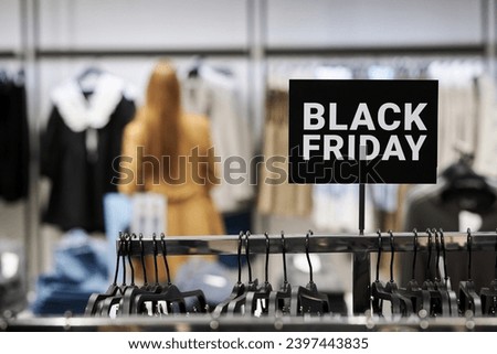 Black friday sign attached to clothing rack at store with customer choosing clothes on background
