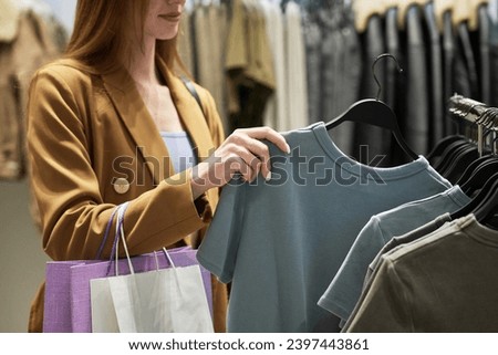 Unrecognizable caucasian girl taking hanger with t-shirt from clothing rack while shopping at store