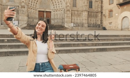 Traveler girl, makes selfie on mobile phone, shows sign of victory while sitting on the steps of an old building in the historical part of an old European city