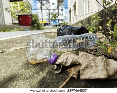 Garbage on the sidewalk, including water bottles and plastic bags, is dirty and blocks the walkway.  It's caused by people not throwing it into the bin. Royalty-Free Stock Photo #2397464857