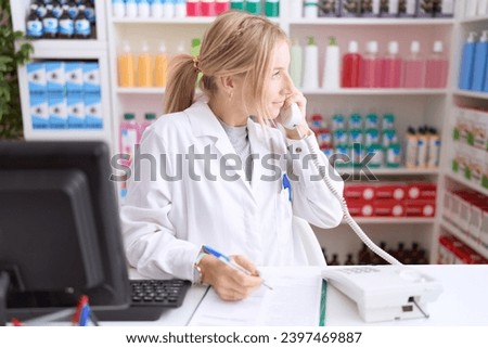 Young caucasian woman working at pharmacy drugstore speaking on the telephone looking to side, relax profile pose with natural face and confident smile. 
