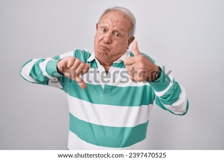Senior man with grey hair standing over white background doing thumbs up and down, disagreement and agreement expression. crazy conflict  Royalty-Free Stock Photo #2397470525