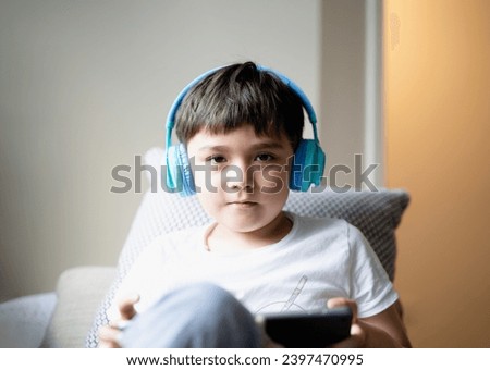 Education concept,High key portrait primary school Kid reading E-book on tablet for homework,Child wearing headphone playing game online on internet,boy sitting on sofa watching cartoon on digital pad