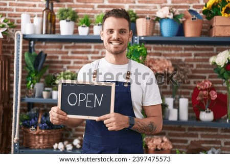 Young hispanic man working at florist holding open sign smiling with a happy and cool smile on face. showing teeth. 