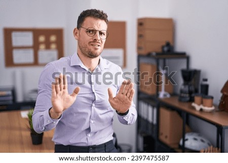 Young hispanic man at the office moving away hands palms showing refusal and denial with afraid and disgusting expression. stop and forbidden.  Royalty-Free Stock Photo #2397475587