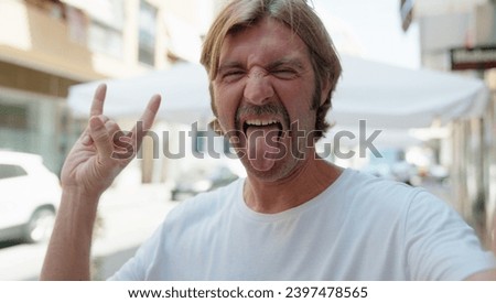 Young blond man smiling confident doing rock sign with fingers at street