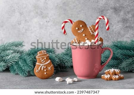 Gingerbread man in a cup with marshmallows and a candy cane, gray background. Christmas symbol. Selective focus. Royalty-Free Stock Photo #2397487347