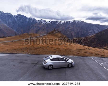 A modern car against the backdrop of very high mountains.