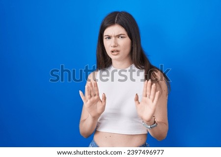 Young caucasian woman standing over blue background moving away hands palms showing refusal and denial with afraid and disgusting expression. stop and forbidden. 