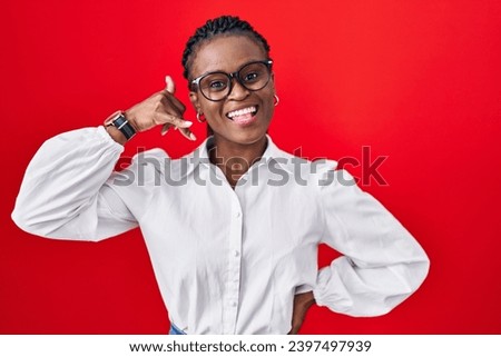 African woman with braids standing over red background smiling doing phone gesture with hand and fingers like talking on the telephone. communicating concepts. 