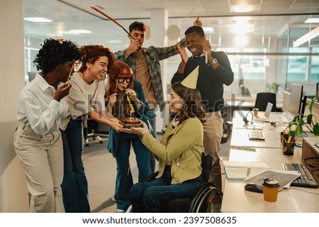 A cheerful inclusive office workers bringing a birthday cake to a colleague with disability and having a surprise party at the office. Birthday celebration and party with coworkers at workspace.