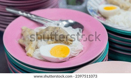 Picture of a type of savory food It's called khanom jeen. In this picture, khanom jeen comes with beaten chicken and half an egg. was placed on the top plate. There is a fork and spoon ready to eat.