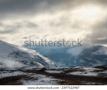 Soft focus. Atmospheric ghostly landscape with fuzzy silhouettes of snow rocks in low clouds. Dramatic view to large mountains blurred in rain haze in gray low clouds with sun rays.
