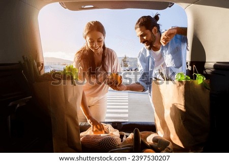 Smiling middle eastern spouses placing fresh produce into the car trunk, sharing a light moment in the warm glow of the evening sun in a parking lot Royalty-Free Stock Photo #2397530207