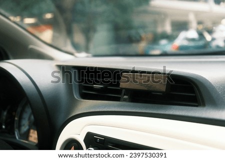 Close-up of a car's dashboard with a wooden air freshener clipped to the air vent, blurred street view in the background