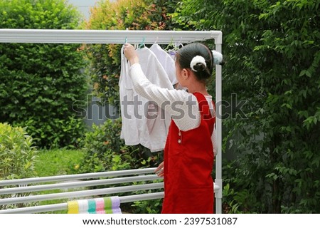 Asian girl child helping to do dry the clothes at the garden near house. Kid hanging cloth on a clothesline. Royalty-Free Stock Photo #2397531087