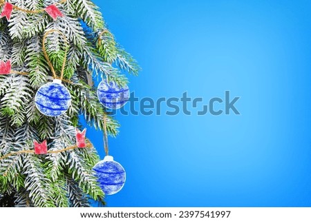 A Christmas tree covered with frost is decorated with paper balls and flags on a blue background. Christmas background with copy space.