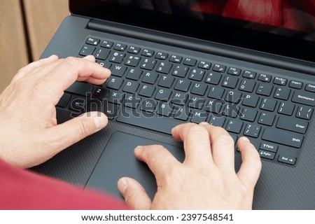 The man's hands on the keyboard of the laptop computer stacked in his lap.                               
