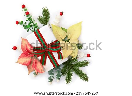Christmas decoration. Gift box, red and white yellow poinsettia flowers, Christmas tree branch, red berries on a white background with space for text. Top view, flat lay